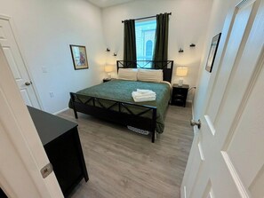 A bedroom with a bed, bedside tables, a window with curtains, a door, and a wall-mounted picture. - Historic Broad St Apt 4 in Upton’s Confectionery (Globe)