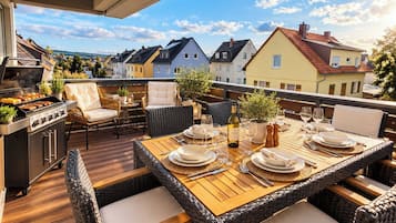 An outdoor dining area with a grill, wicker furniture, and a view of neighboring houses.