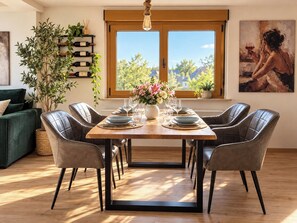 A dining area with a wooden table set for six, surrounded by leather chairs, with a large window offering a view of trees and houses. - New Listing (Oestrich-Winkel)