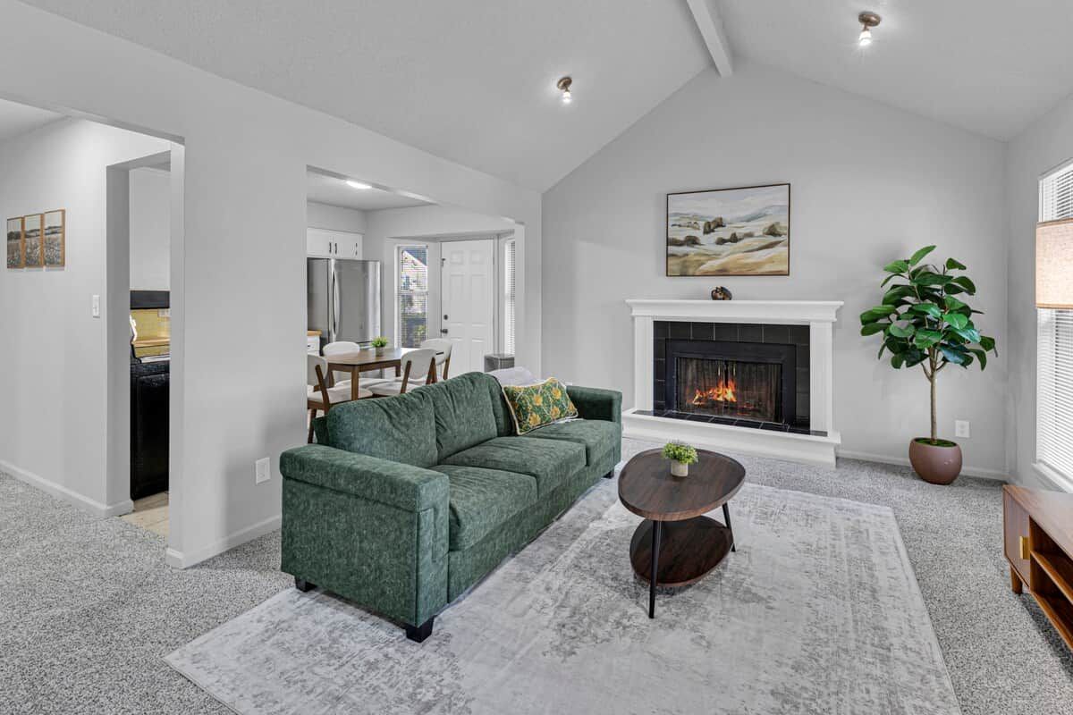 A living room with a green sofa, a fireplace, and a dining area in the background.