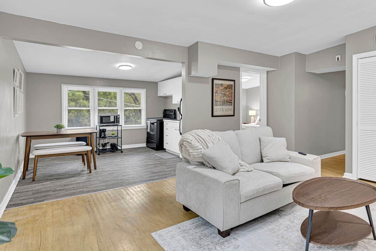 A modern living room with a grey sofa, a round coffee table, and a dining area with a bench and a small table.