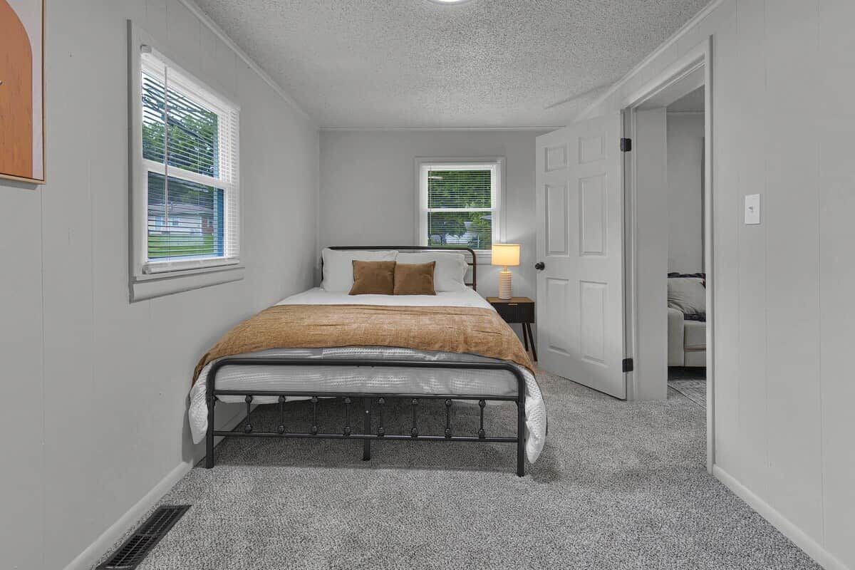 A bedroom with a bed, a nightstand, and a door leading to another room.