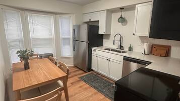 A compact kitchen with white cabinets, a black refrigerator, a dining table with chairs, and a black stove.
