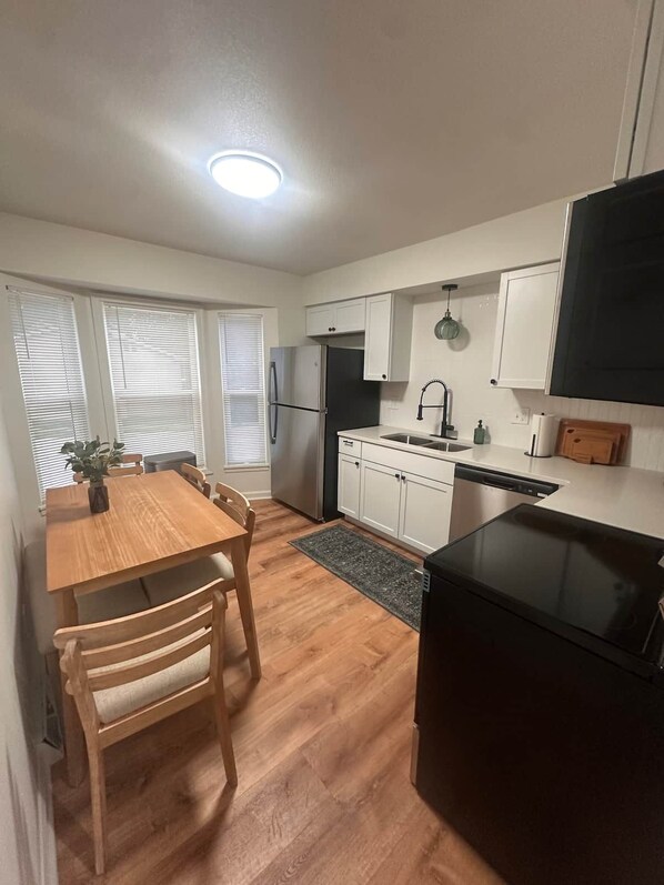 Cocina compacta con armarios blancos, un refrigerador negro, una mesa de comedor con sillas y una estufa negra.