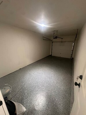 Una habitación con piso gris moteado, un ventilador de techo, una puerta blanca con llave en la cerradura y una pared blanca.