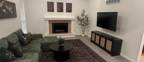 A living room with a sectional sofa, a fireplace, a television, and a decorative plant.
