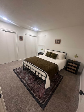 Un dormitorio con cama, mesitas de noche, una alfombra y un cuadro en la pared.