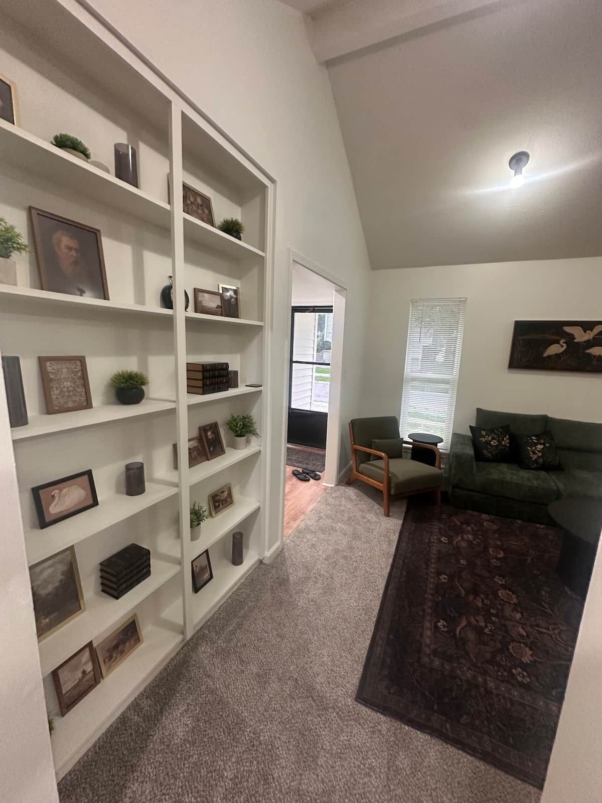 A living room with a bookshelf, a green sofa, a patterned rug, and a painting on the wall.