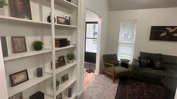 A living room with a bookshelf, a green sofa, a patterned rug, and a painting on the wall.