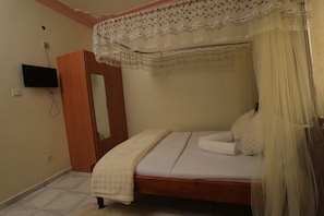 A bedroom with a bed, a television mounted on the wall, and a wooden wardrobe. - Grand view motel Fort Portal (Fort Portal)