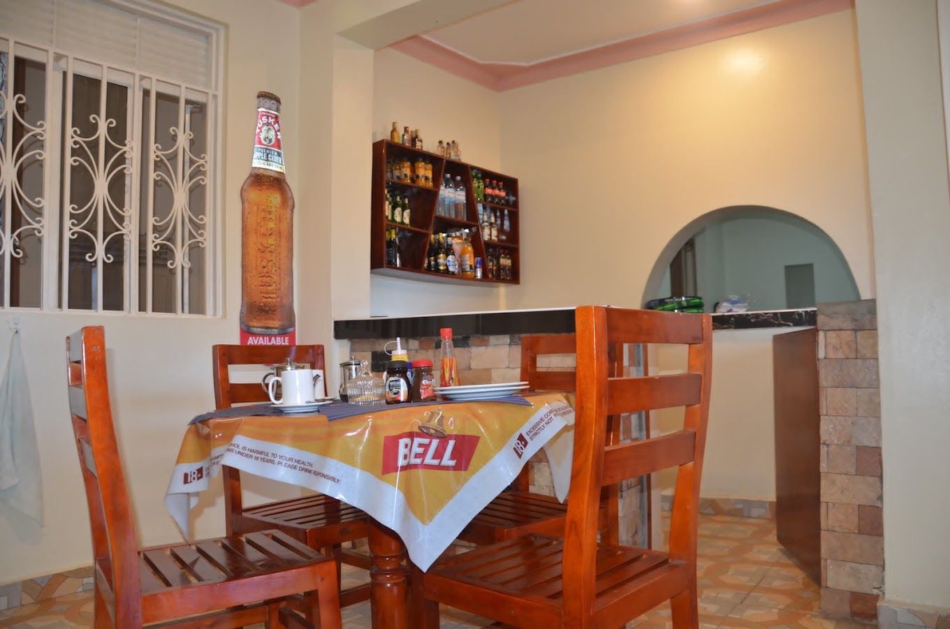 A dining area with a table set for two, a bottle of whiskey, and a shelf with various bottles.