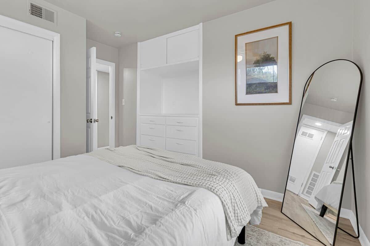 A bedroom with a bed, a wardrobe, a mirror, and a framed picture on the wall.