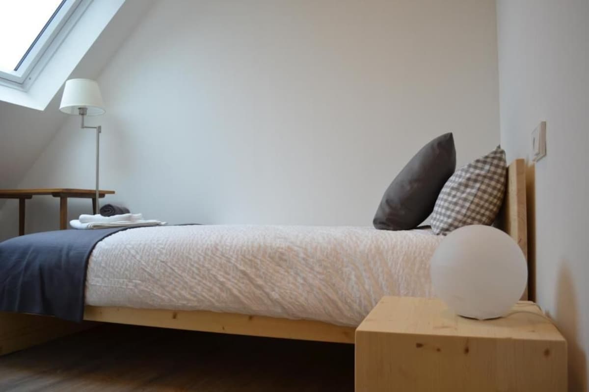 Un dormitorio con cama, mesita de noche, lámpara y vista al cielo a través de un tragaluz.