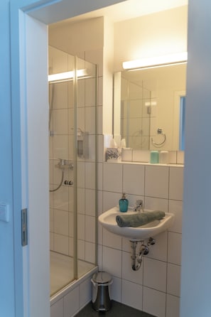 Un baño con cabina de ducha de vidrio, un lavabo con toalla y un espejo sobre el lavabo.