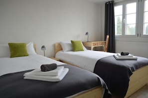 Dos camas individuales con ropa de cama blanca y negra, almohadas verdes y una mesita de noche de madera con una lámpara entre ellas.