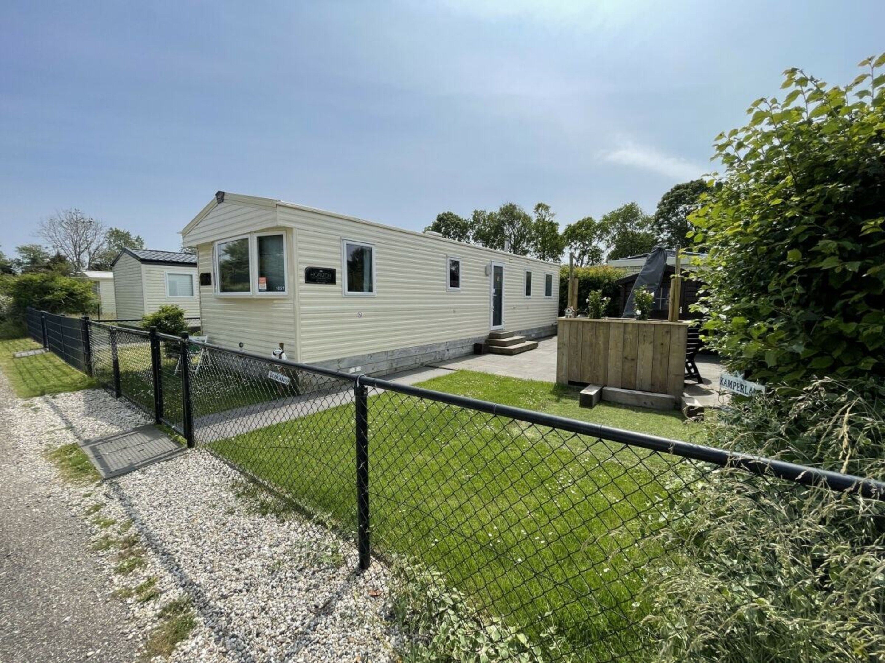 A mobile home with a fenced yard, a small deck, and a gravel path leading to the entrance.