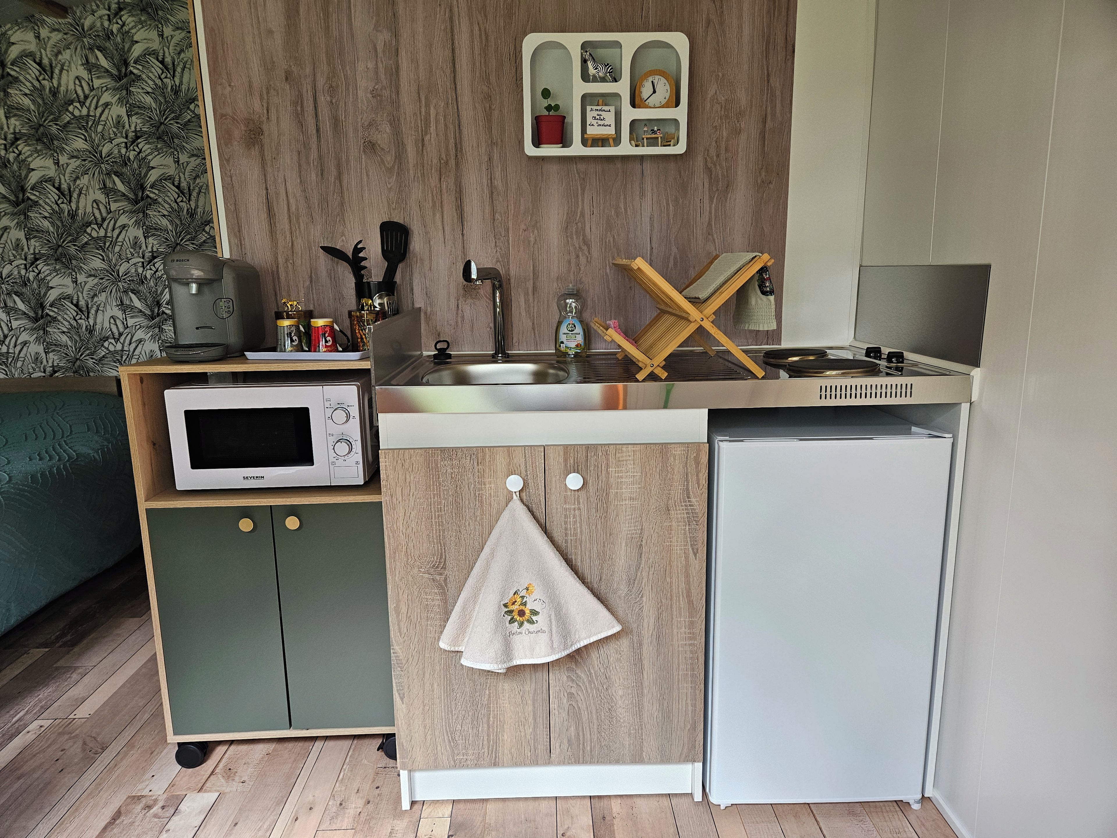 Een kleine keuken met een magnetron, kookplaat, spoelbak en een kleine koelkast.