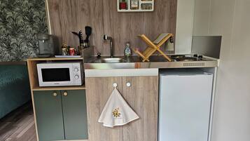 Een kleine keuken met een magnetron, kookplaat, spoelbak en een kleine koelkast.