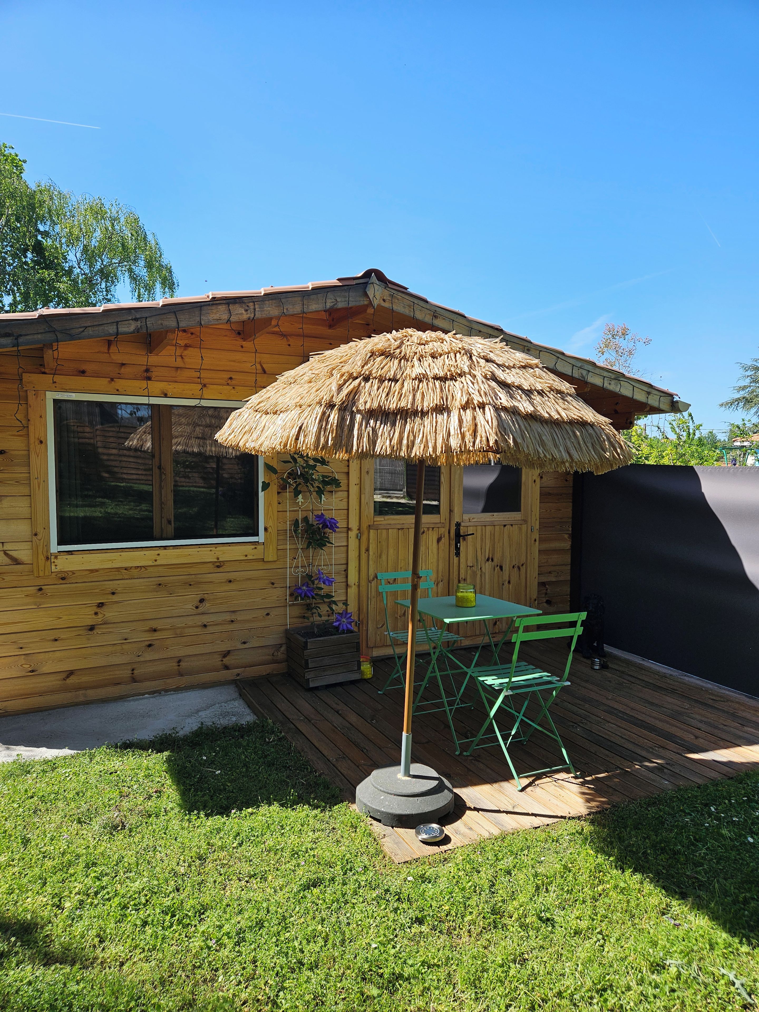 Een houten chalet met rieten dak, een raam en een tafel met stoelen buiten.