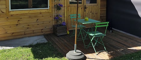 A wooden cabin with a thatched roof, a window, and a table with chairs outside.