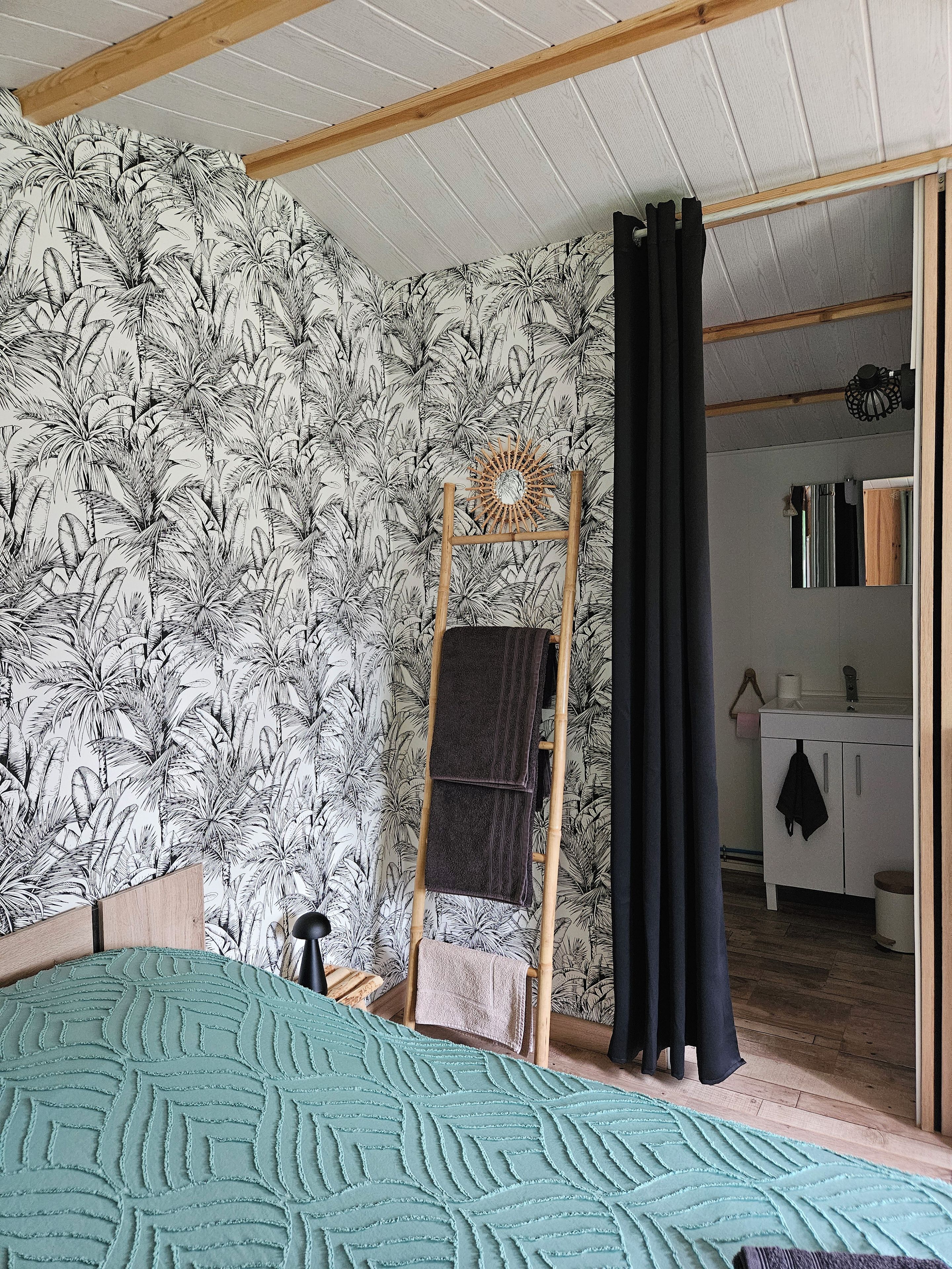 Een kamer met een bed, een houten trap, een badkamer met een spiegel en een behang met een patroon.