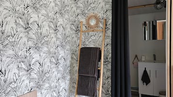 Una stanza con un letto, una scala in legno, un bagno con uno specchio e un muro decorato.
