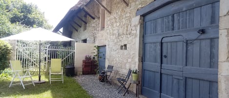 A stone building with a large wooden garage door, a covered patio with chairs and a table, and a gravel pathway.