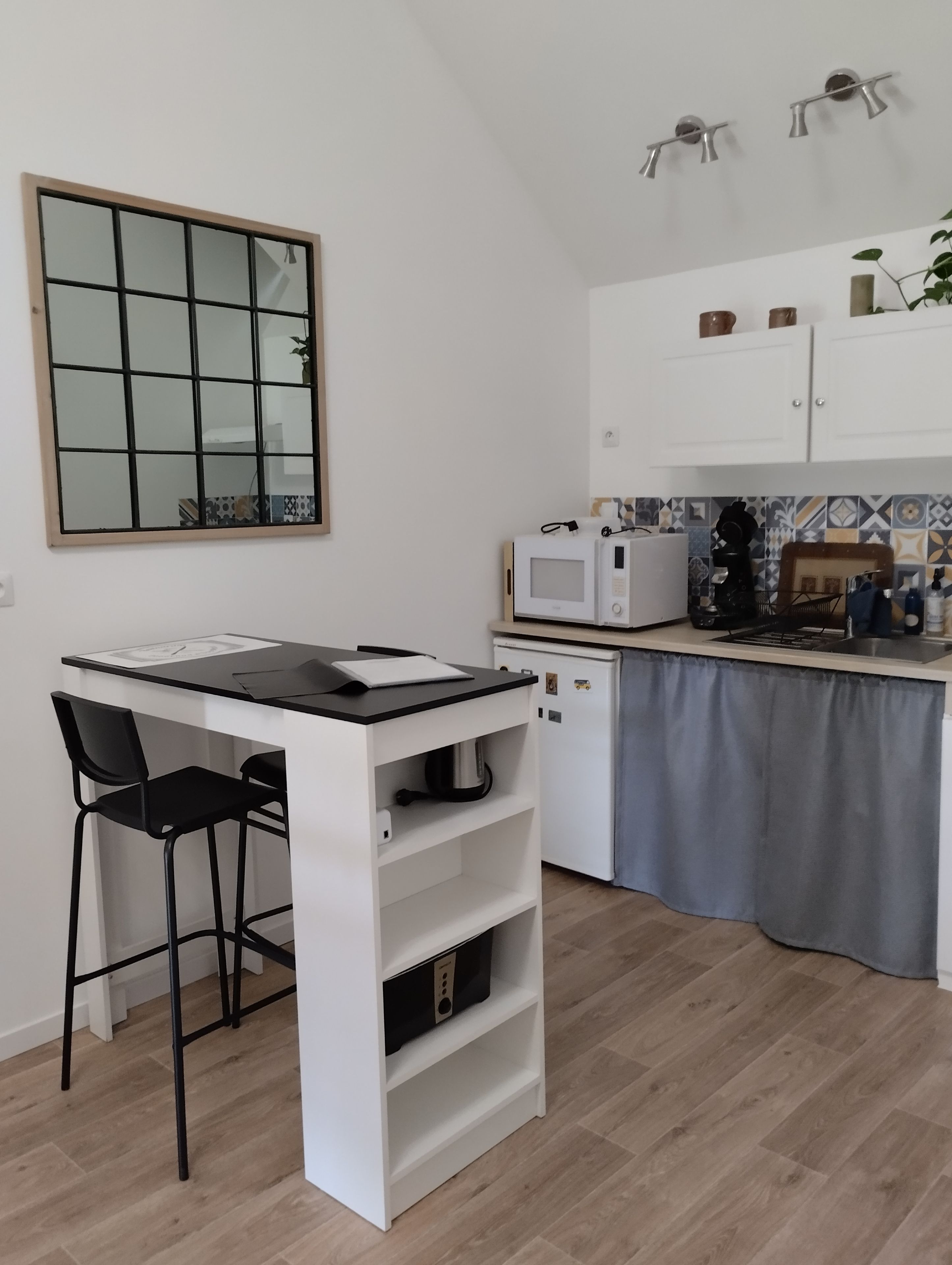 Une cuisine compacte dotée d’un plan de travail blanc, d’un four à micro-ondes, d’une bouilloire et d’un petit réfrigérateur.
