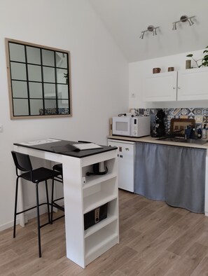 Une cuisine compacte dotée d’un plan de travail blanc, d’un four à micro-ondes, d’une bouilloire et d’un petit réfrigérateur.