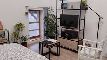 Un dormitorio moderno con cama, televisor en estante, mesita y silla blanca.