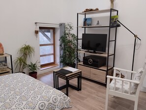 Une chambre moderne avec un lit, un téléviseur posé sur une étagère, une petite table et une chaise blanche.