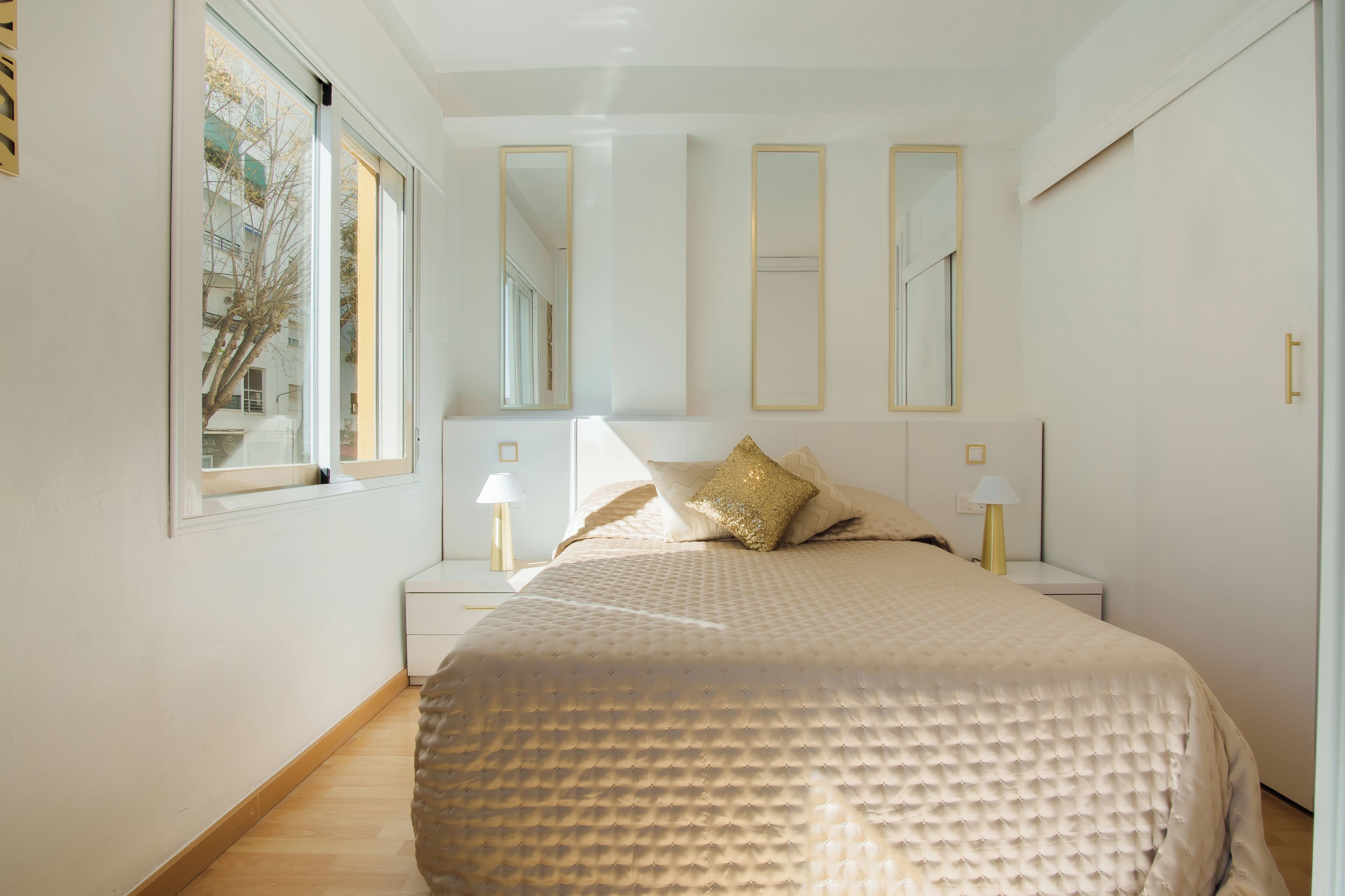 Un dormitorio con una cama grande, dos mesitas de noche con lámparas y tres espejos en la pared.