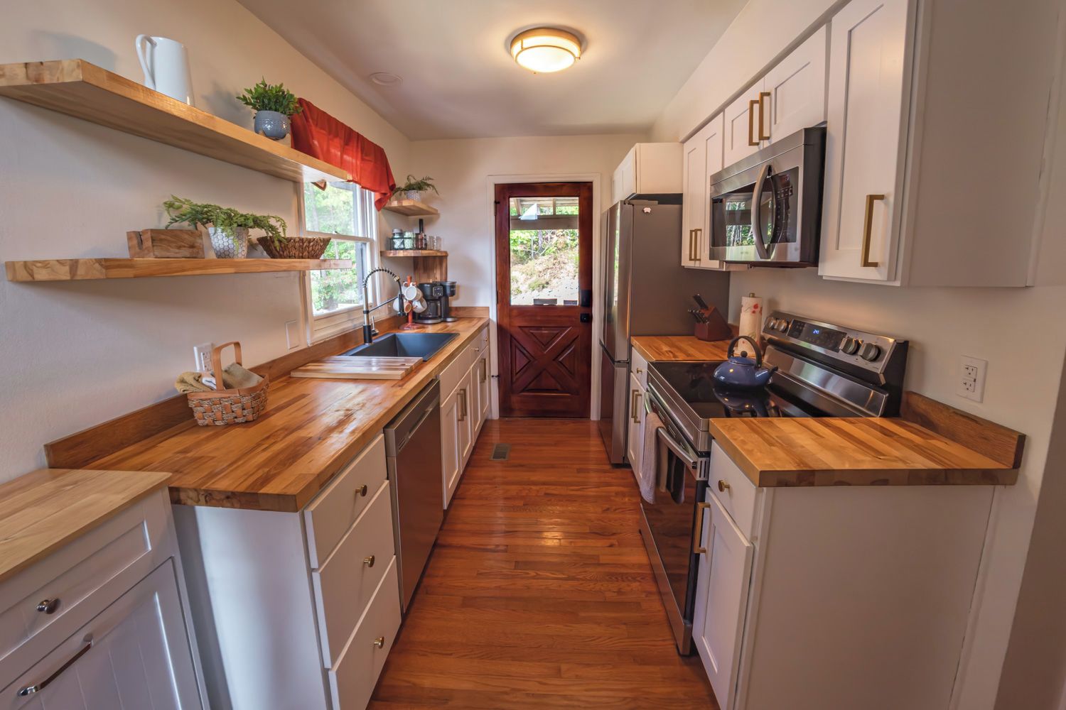 A narrow kitchen with wooden countertops, white cabinets, a stainless steel refrigerator, and a built-in oven.