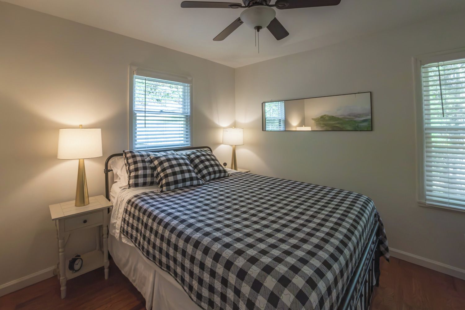 A bedroom with a bed, two bedside lamps, a ceiling fan, and a window with blinds.