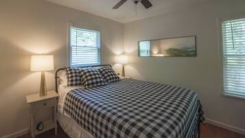 A bedroom with a bed, two bedside lamps, a ceiling fan, and a window with blinds.