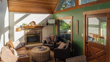 A cozy living room with a fireplace, comfortable seating, and a view through a glass door.