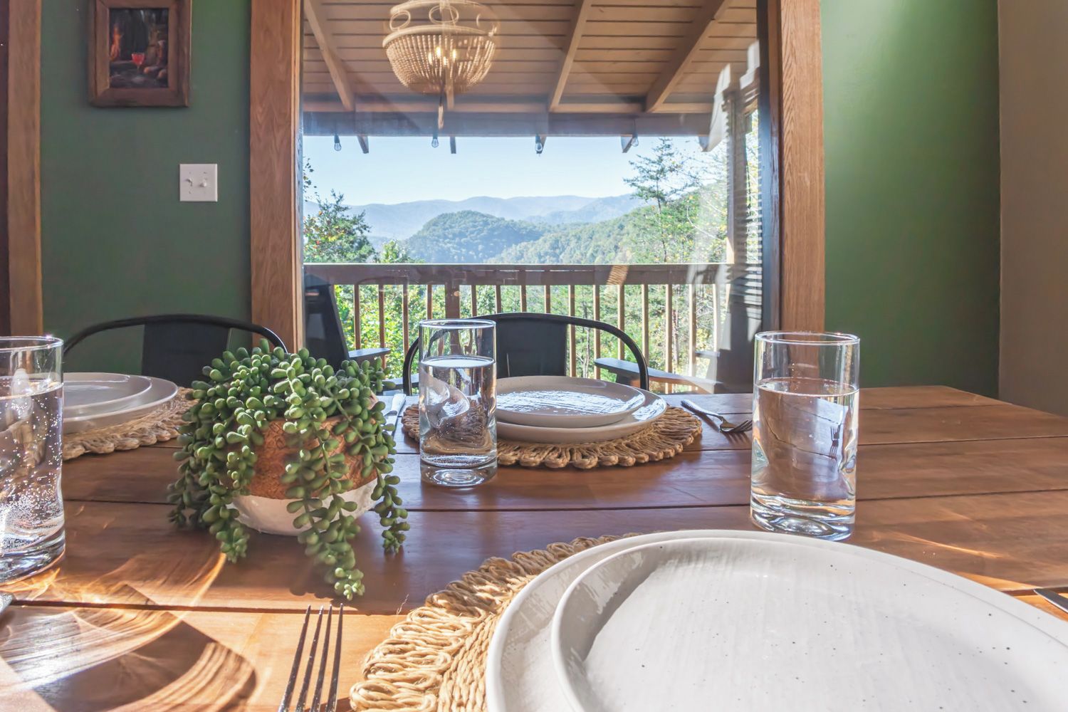 A dining table set with plates, glasses, and a potted plant, overlooking a mountainous landscape.
