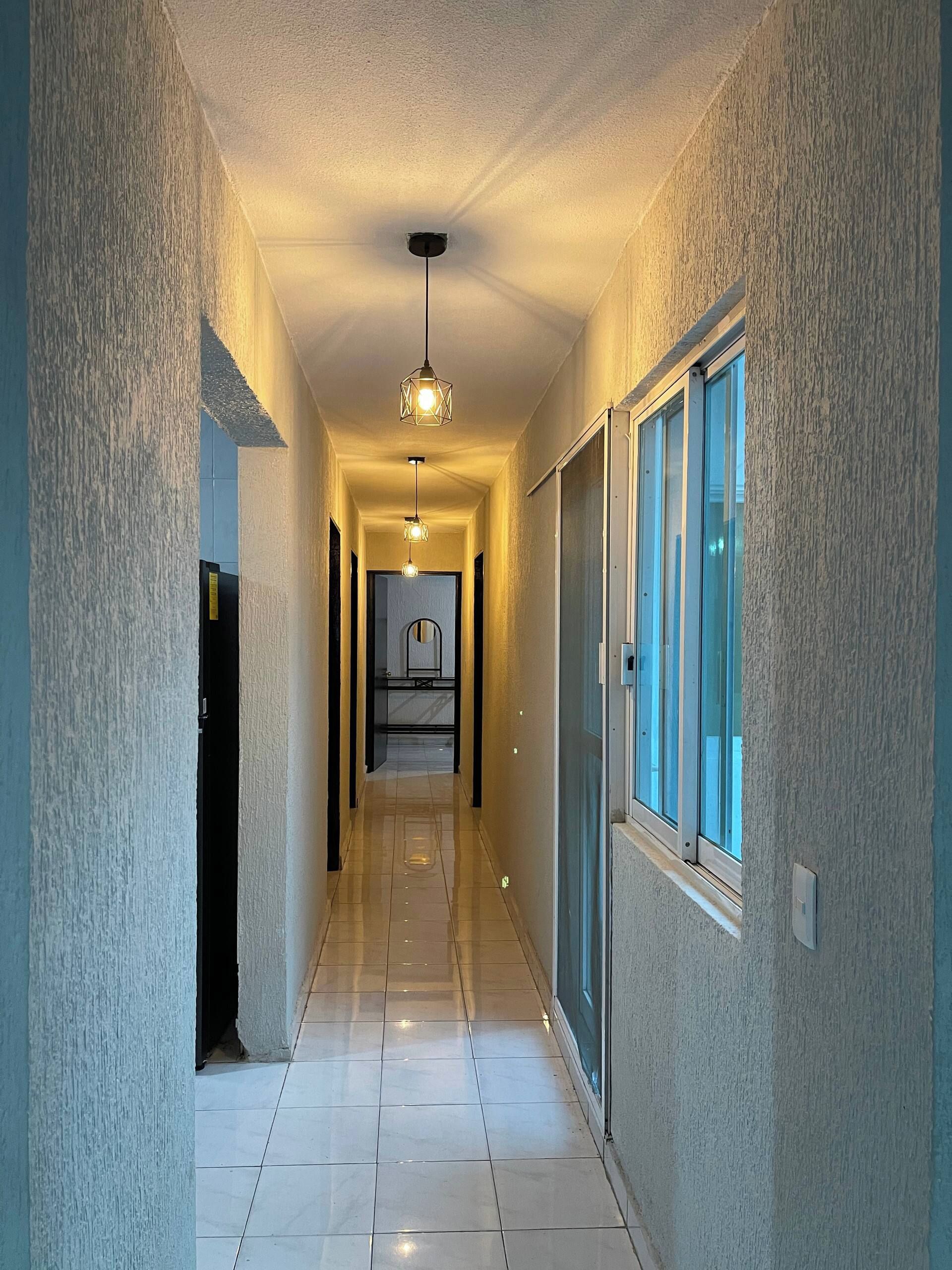 A corridor with a ceiling light fixture, a door on the left, and a window on the right.