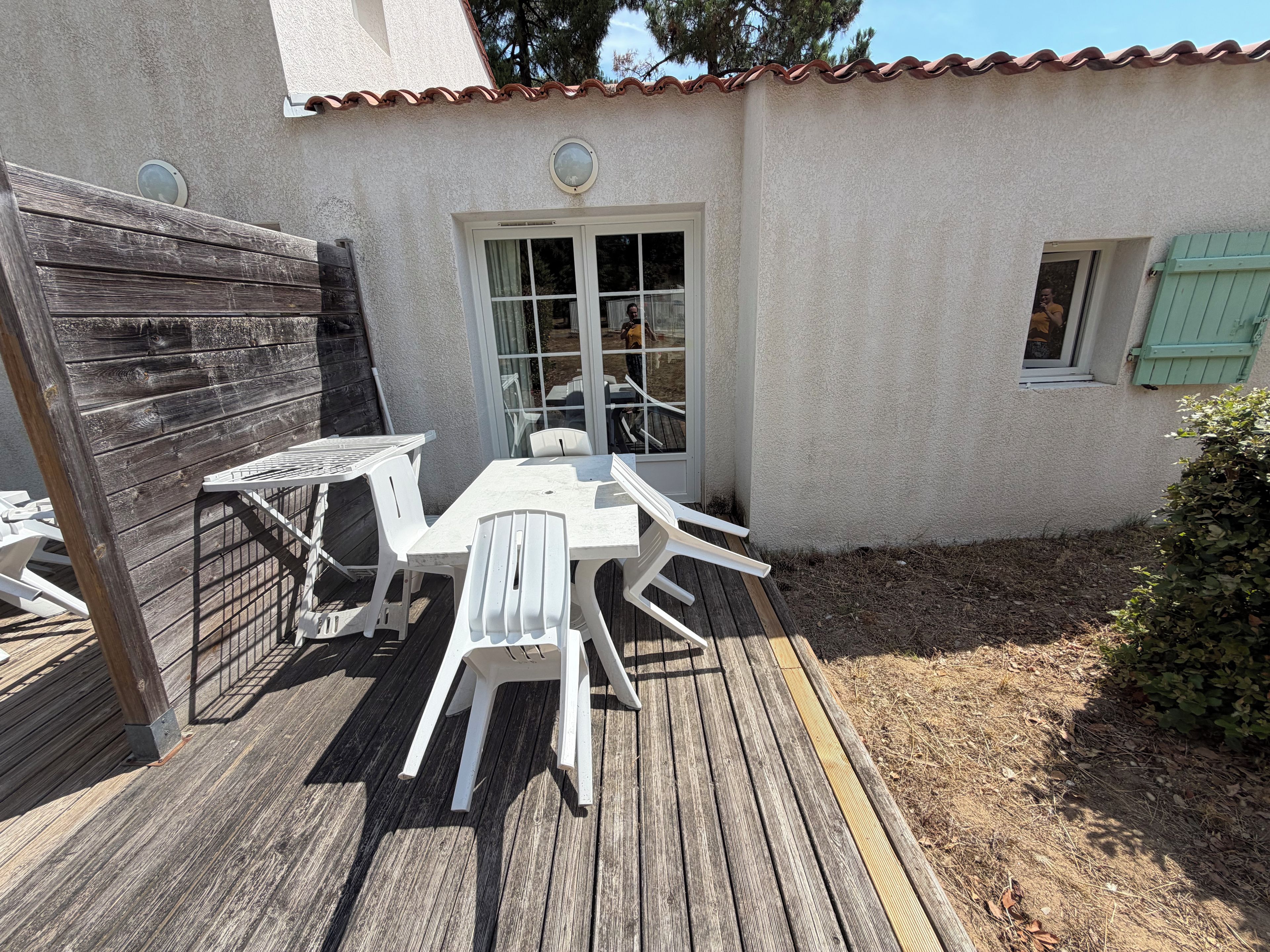 Une terrasse avec une plateforme en bois, des chaises en plastique blanches et une table.