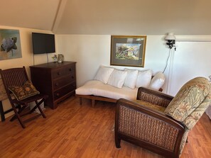 Ein gemütliches Wohnzimmer mit einer Couch, zwei Sesseln, einer Holzkommode und einem Bild an der Wand.