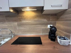 Een keuken met een zwart inductiekookplaatje, een koffiezetapparaat en een mandje koffiecups.