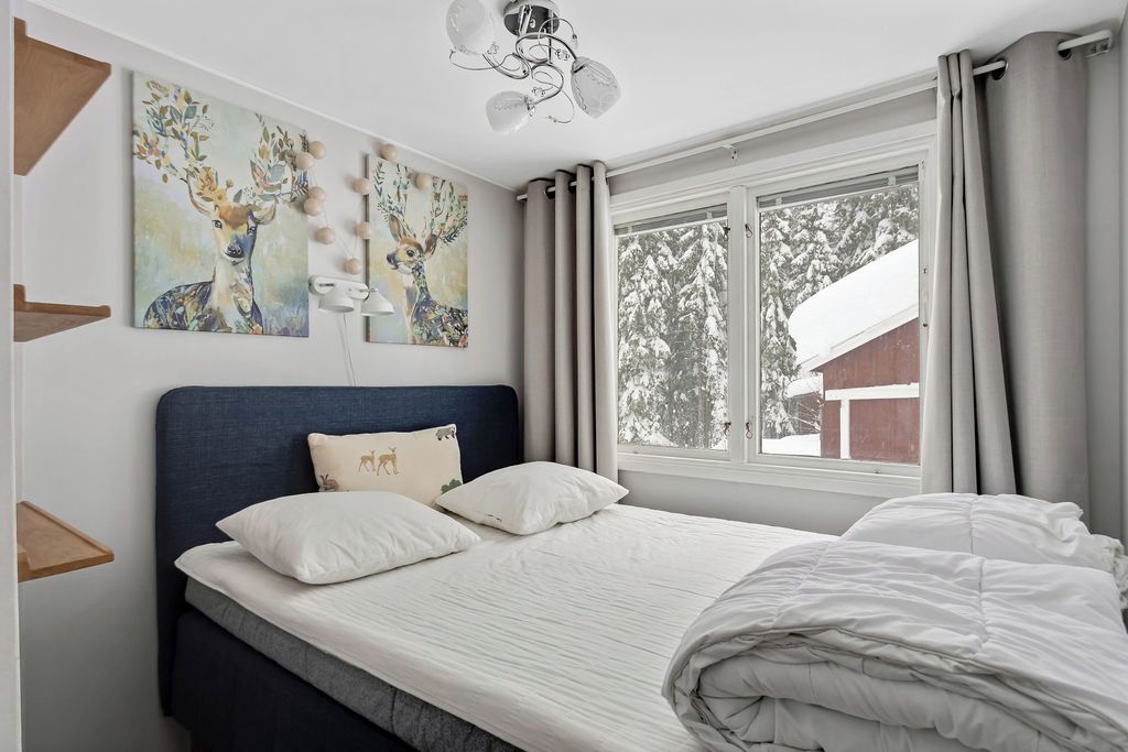 A bedroom with a bed, a headboard, a window with curtains, and wall art.