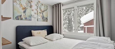 A bedroom with a bed, a headboard, a window with curtains, and wall art.