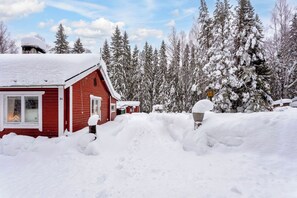 Une cabane rouge, dont le toit est recouvert de neige, entourée d’arbres chargés de neige.