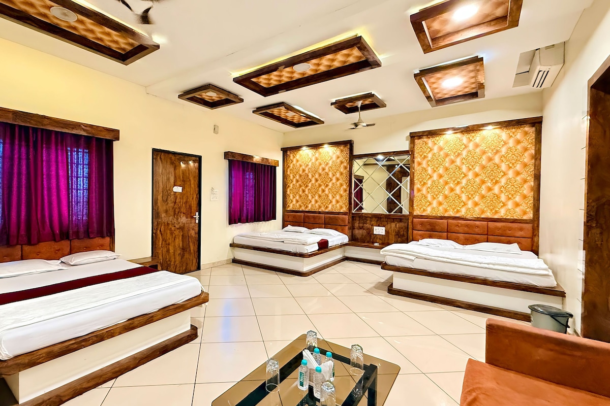 A hotel room with three beds, a small table with bottles, and a mirror.