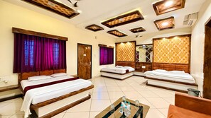 A hotel room with three beds, a small table with bottles, and a mirror. - Maa Vaishnavi New Restaurant & Hotel (Omkareshwar)