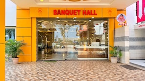Un salón de banquetes con entrada de vidrio, plantas en macetas y piso de baldosas.