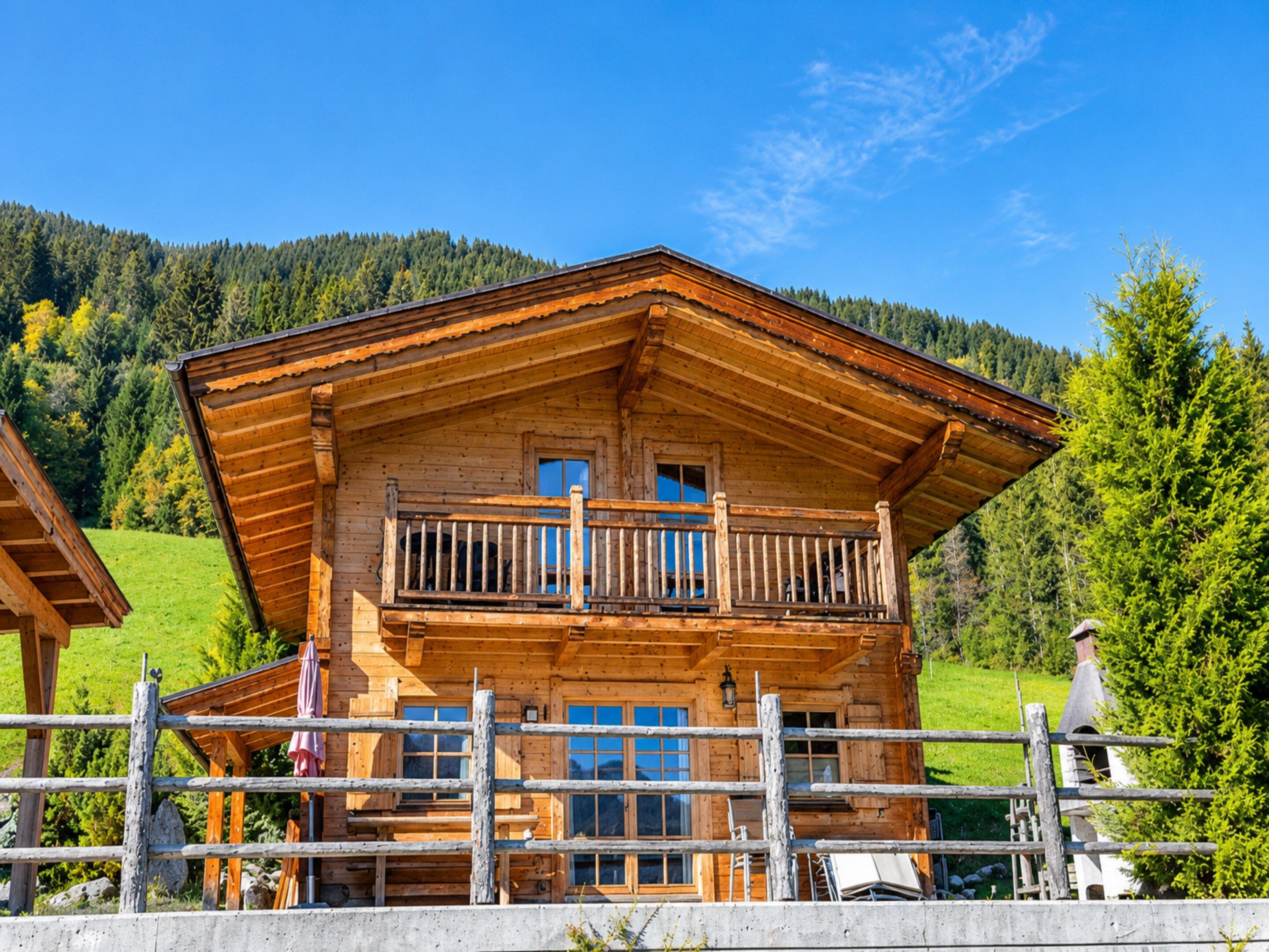 Un chalet en bois doté d’un balcon, entouré d’une clôture en bois, se dressant sur un fond de collines verdoyantes et d’un ciel dégagé.