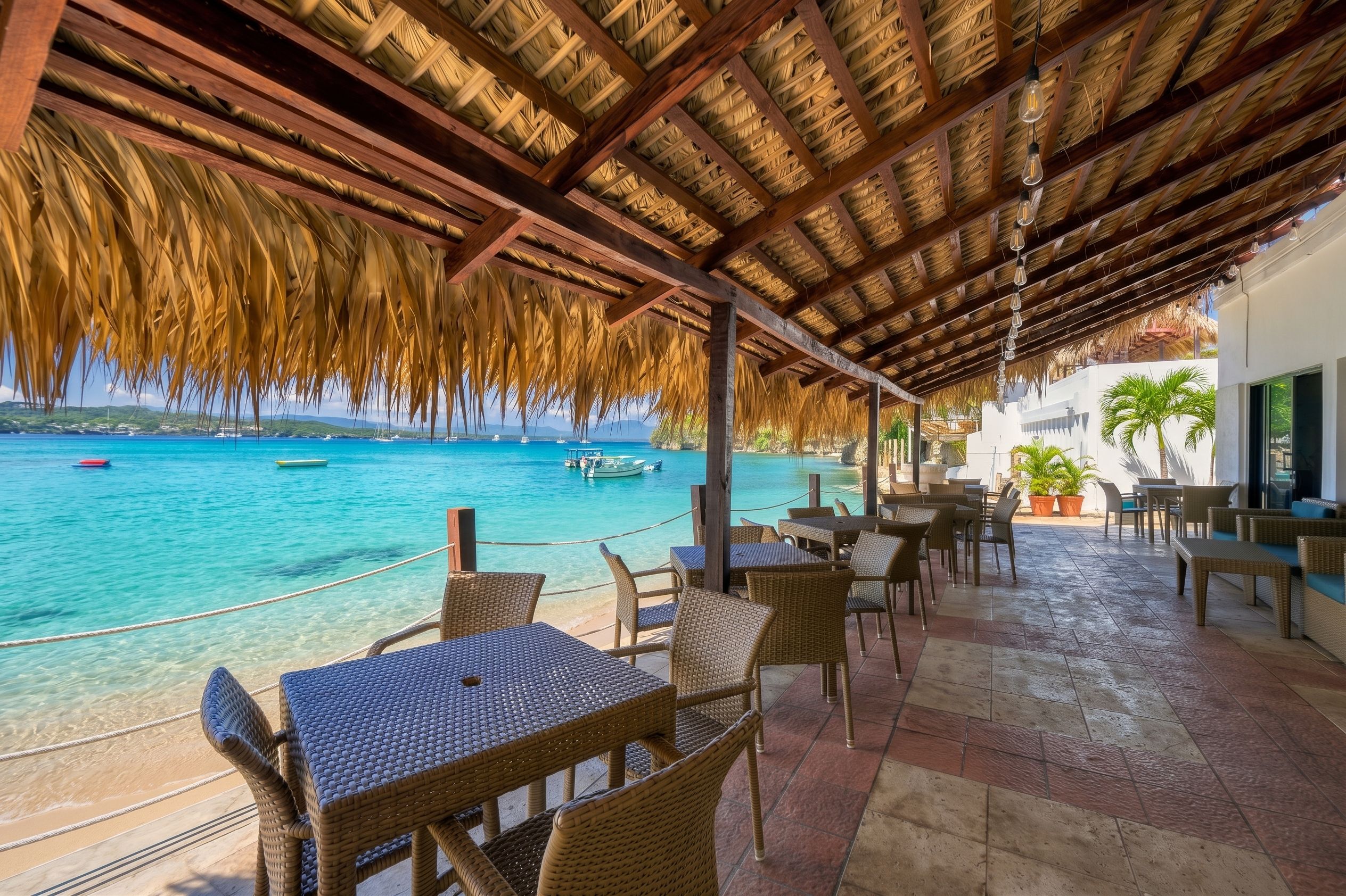 A covered outdoor seating area with wicker furniture overlooking a clear blue sea.