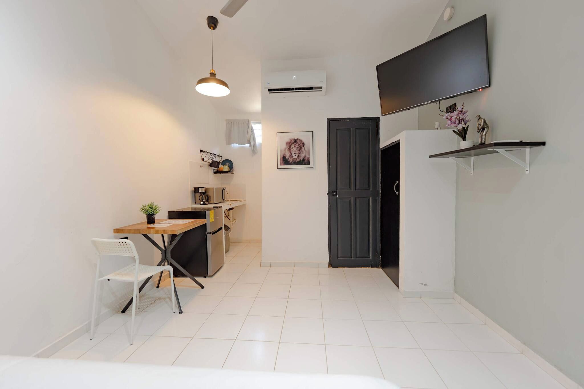 A compact living space with a kitchenette, a dining area, and a TV mounted on the wall.